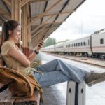 Asian female traveler using her smart phone mobile while waiting for a train at a station