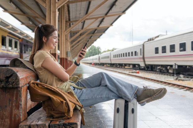 Asian female traveler using her smart phone mobile while waiting for a train at a station