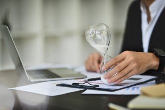 Professional businessman with hourglass sitting at office desk. Business and time management concept