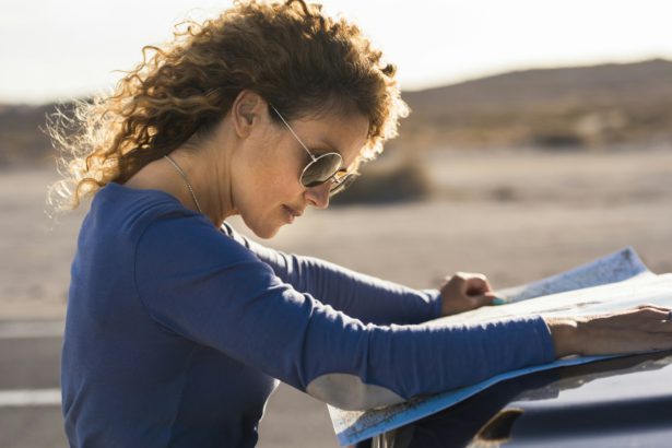 Single woman enjoy travel adventure reading map on the car outdoor on the road. Adult female